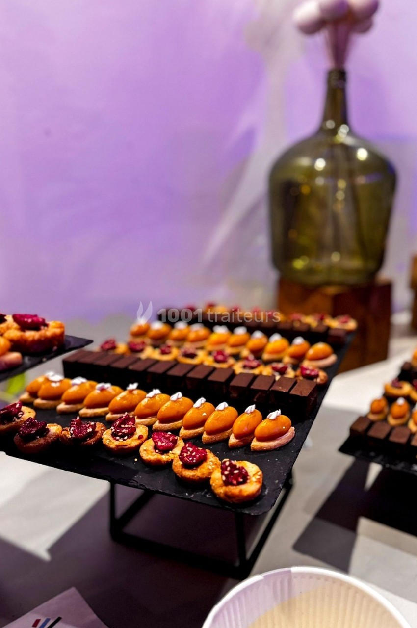 Plateaux de mignardises variées, incluant des chocolats et des pâtisseries fruitées, disposés sur des supports noirs.