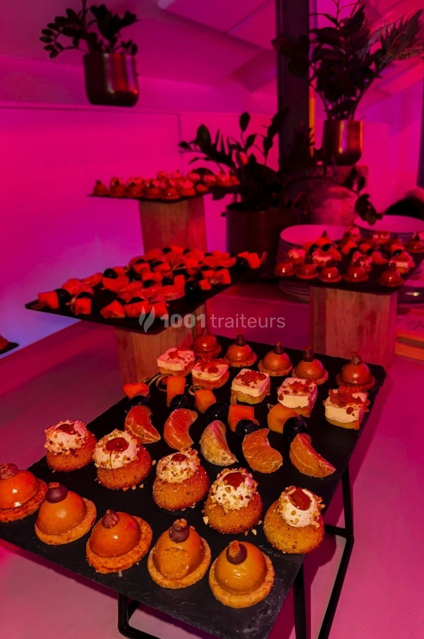 Plateaux de desserts variés présentés sur des ardoises dans une ambiance lumineuse rose et rouge.