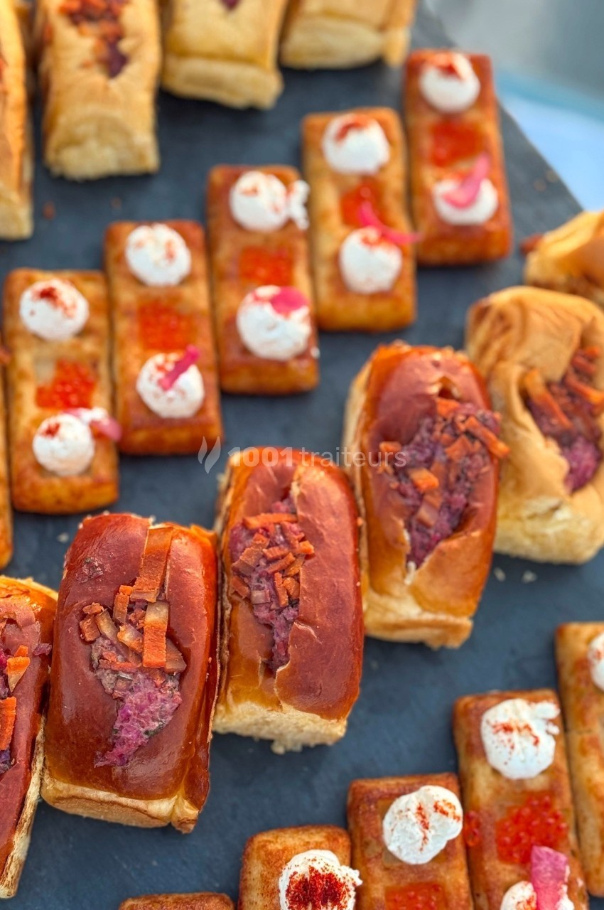 Assortiment de bouchées salées sur ardoise, incluant pains garnis et canapés décorés de crème et œufs de poisson.