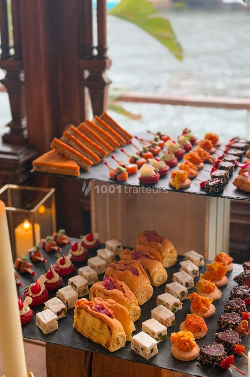Plateaux de canapés variés avec des bouchées salées et sucrées, présentés sur des ardoises près d'une fenêtre.