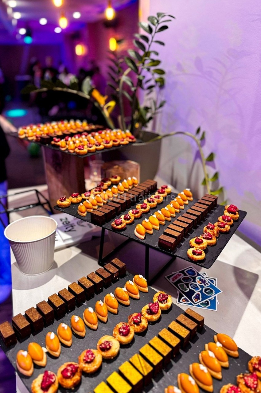 Plateaux de mignardises variées disposés sur une table, avec un décor lumineux en arrière-plan.