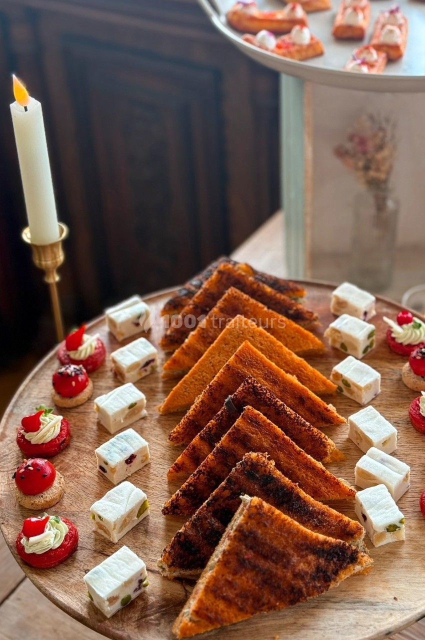 Plateau en bois avec toasts grillés, bouchées sucrées rouges et cubes de fromage, disposés de manière symétrique.