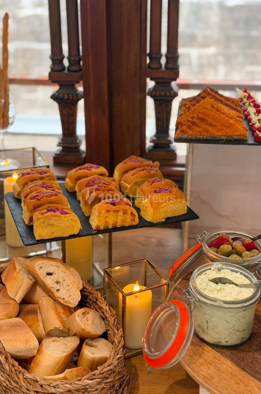Buffet avec pains variés, focaccias garnies, tartines, bougies décoratives et condiments dans un cadre chaleureux.