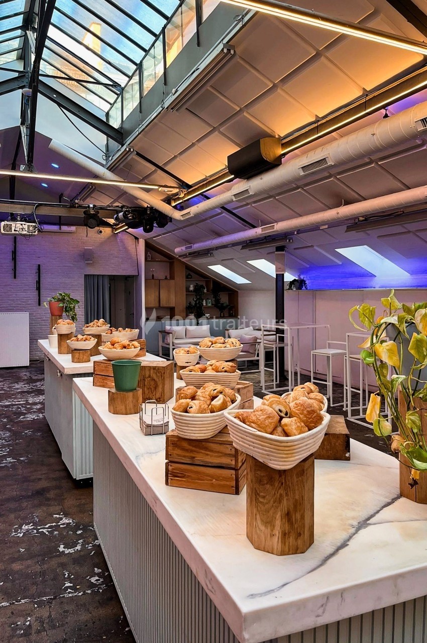 Buffet de viennoiseries disposé sur une table en marbre dans un espace lumineux avec verrière et éclairage moderne.