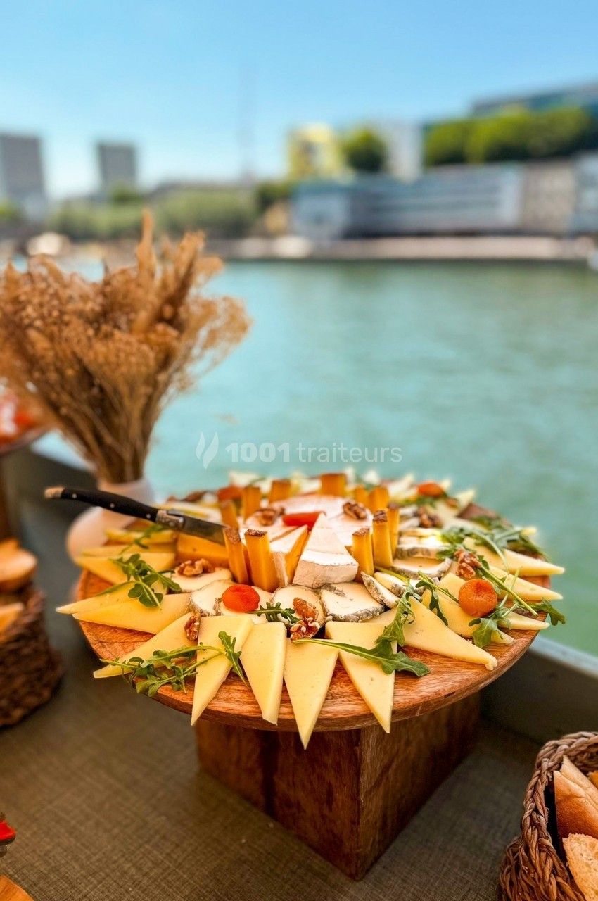 Plateau de fromages variés avec décorations de noix et roquette, présenté sur une table en bord de rivière.