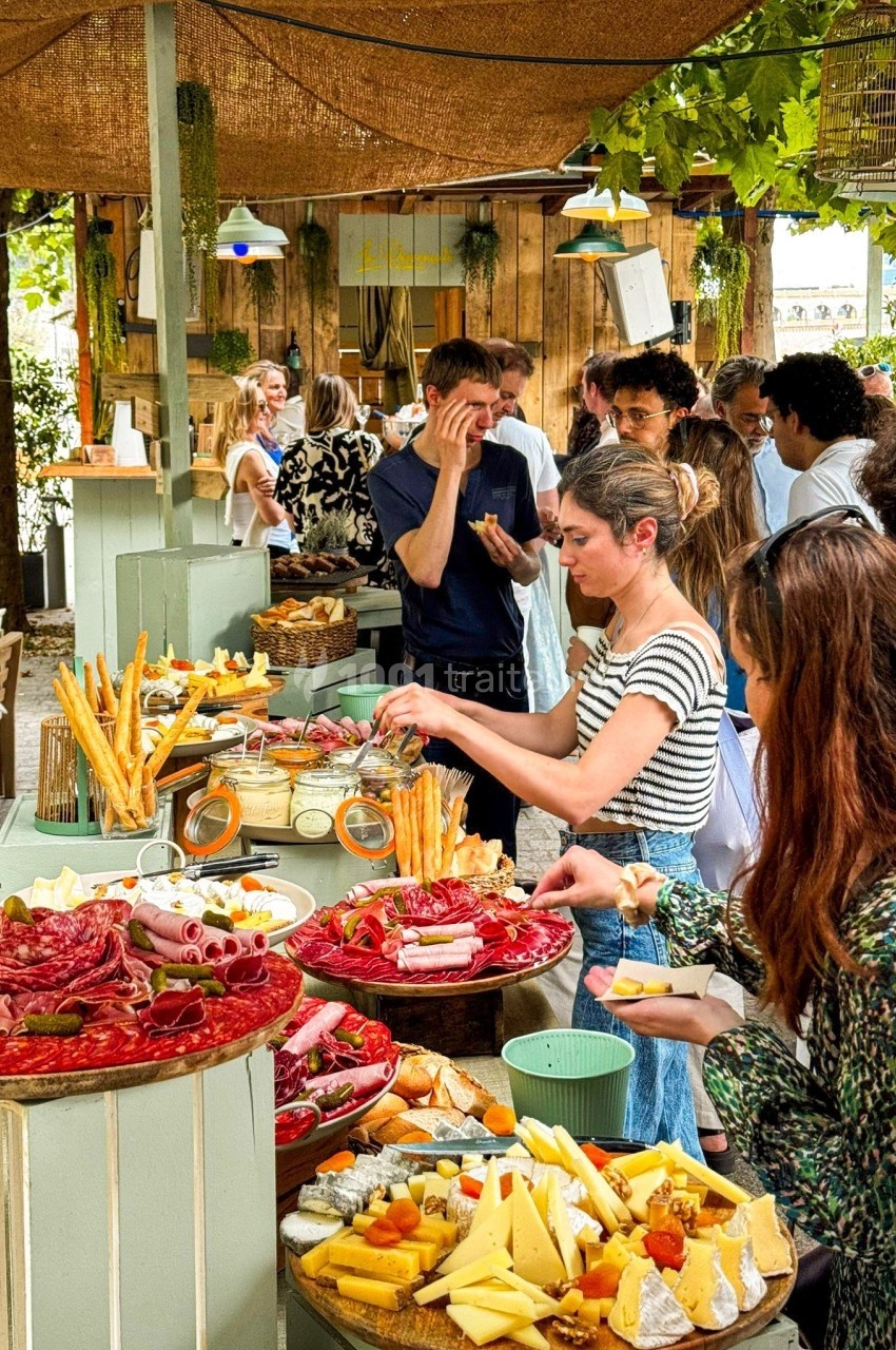Buffet en plein air avec des plateaux de charcuterie, fromages et pains, entouré de convives se servant.
