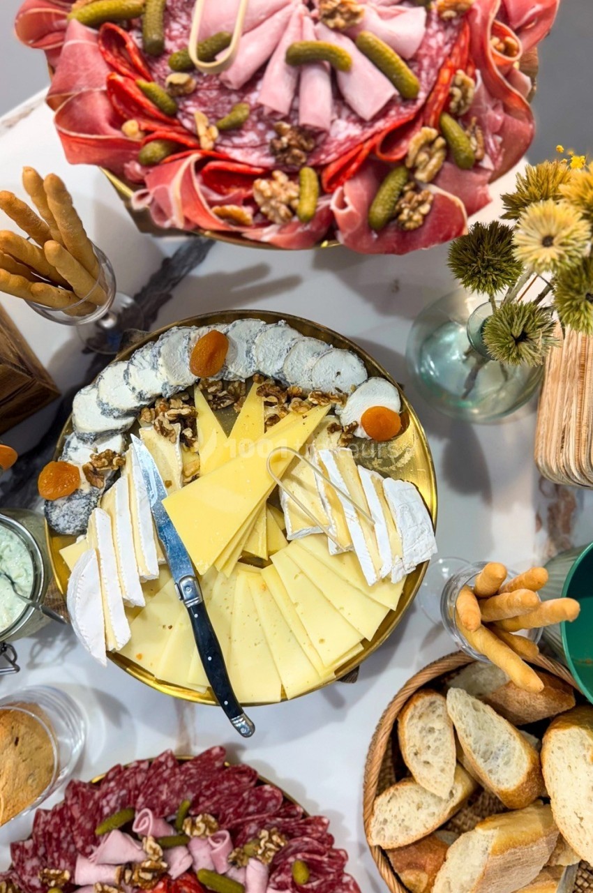 Plateau de fromages et charcuteries variées avec pains, gressins et décorations sur une table.