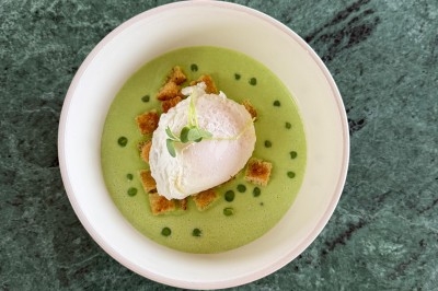 Bol de soupe verte garnie d'un œuf poché, de croûtons et d'une herbe fraîche, posé sur une table en marbre vert.
