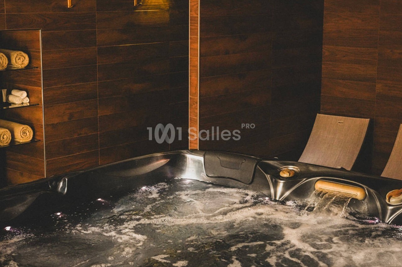 Bain à remous avec eau bouillonnante, chaises longues en bois et étagère contenant des serviettes pliées.