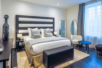 Chambre lumineuse avec lit double, bureau, télévision, grande fenêtre et salle de bain attenante visible.