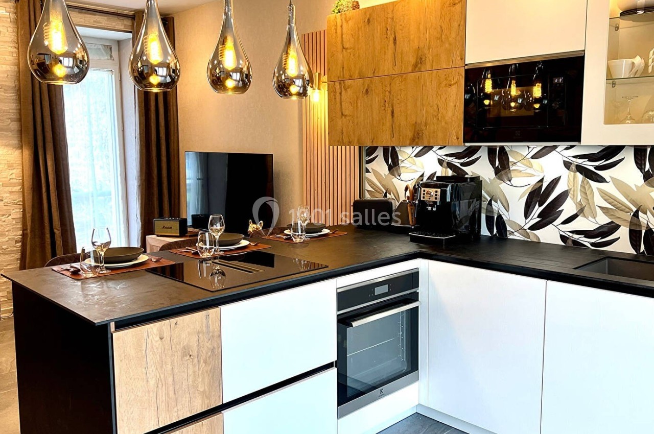 Cuisine moderne avec îlot central, meubles en bois et blanc, crédence à motifs végétaux et luminaires suspendus.