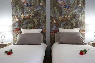Lit à baldaquin blanc avec drapé, fauteuil rose et mur décoré de motifs floraux dans une chambre lumineuse.