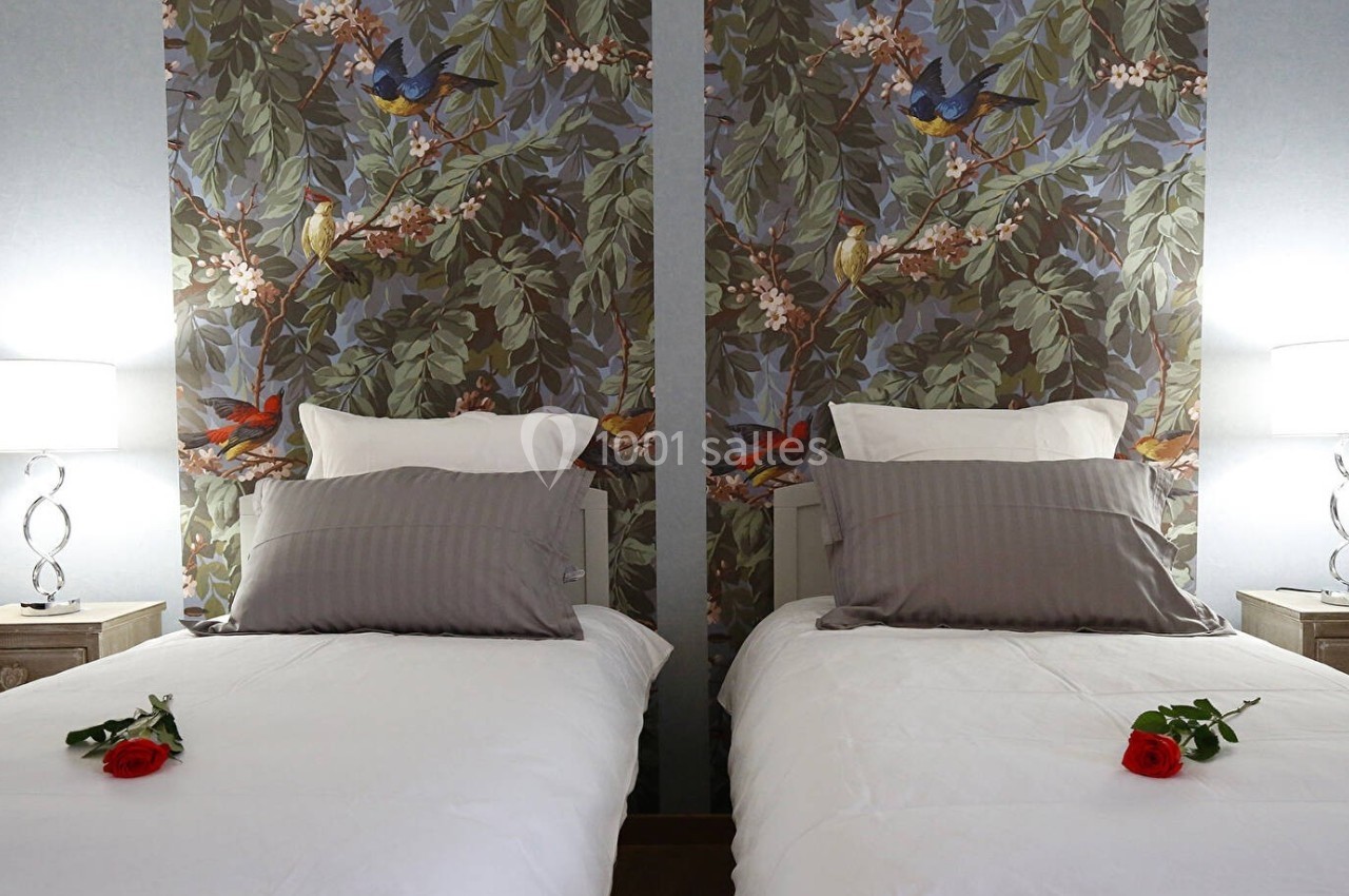 Deux lits simples avec linge blanc, coussins gris, roses rouges sur chaque lit et lampes allumées de chaque côté.