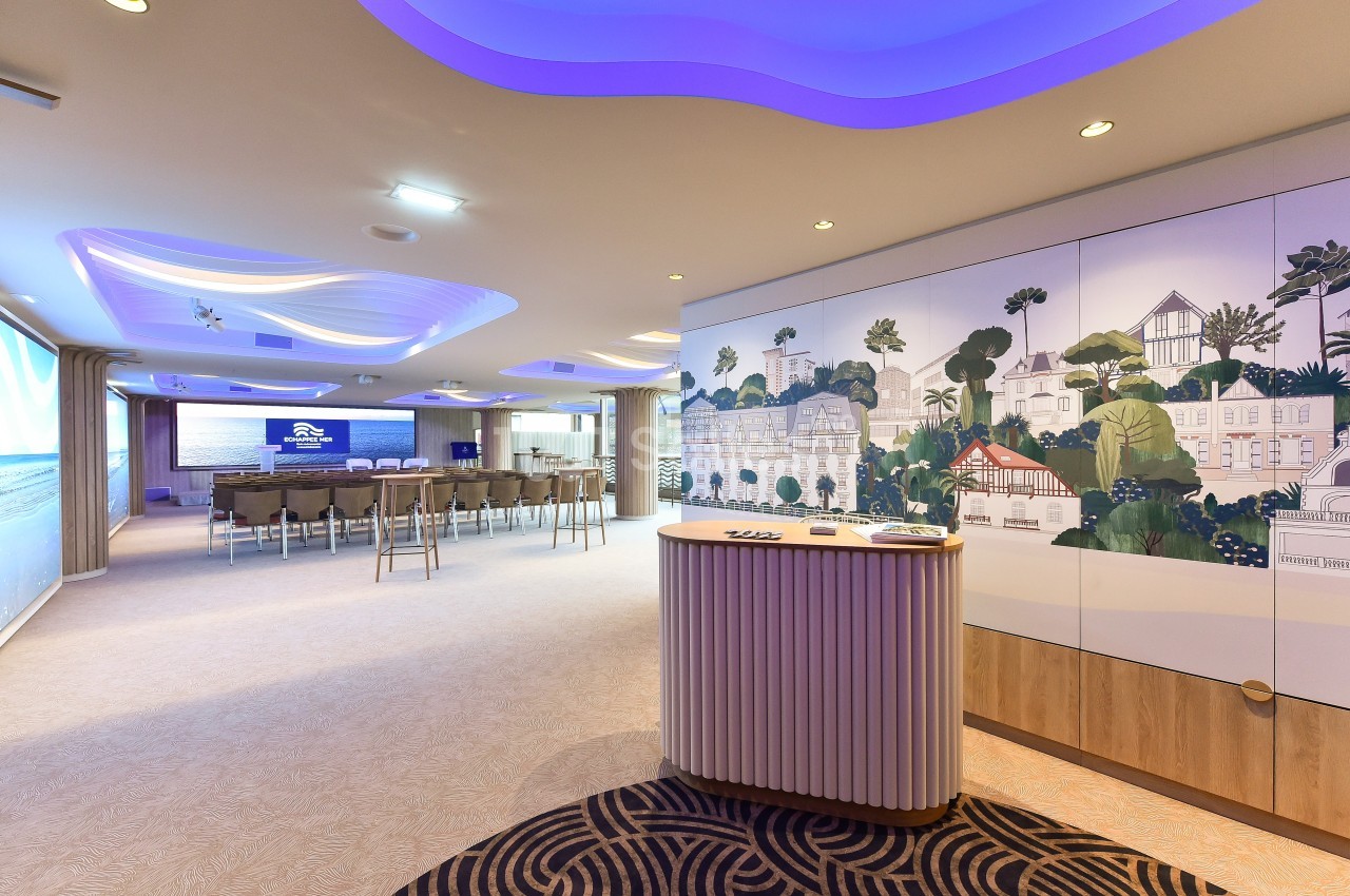 Salle de conférence lumineuse avec chaises alignées, écran de présentation et mur décoré d'une fresque colorée.