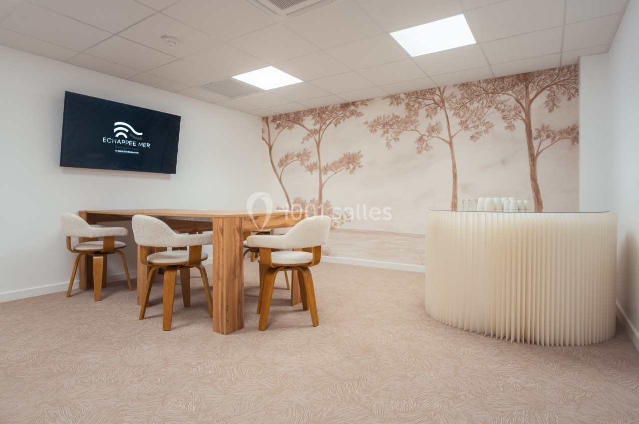 Salle de réunion lumineuse avec table en bois, chaises rembourrées, mur décoré d’un motif nature et écran mural.