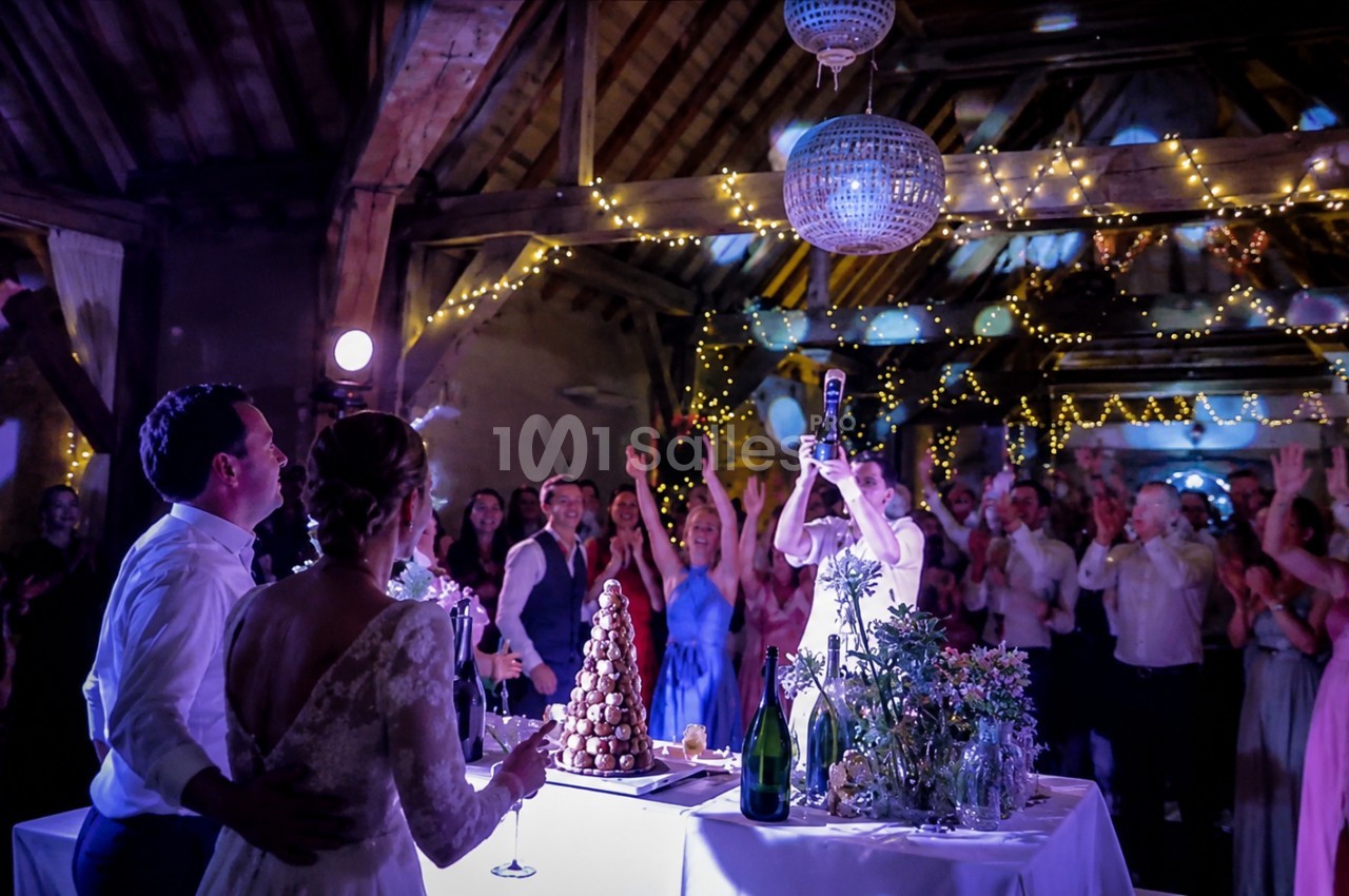 Un couple de mariés regarde leurs invités célébrer dans une salle décorée de guirlandes lumineuses.