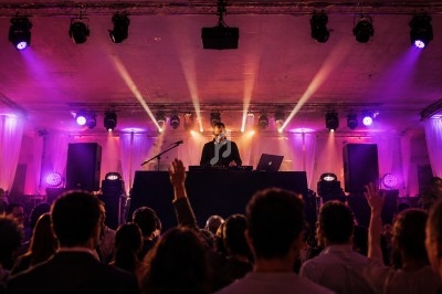 Un DJ mixe sur scène sous des éclairages colorés, face à une foule dans une ambiance festive.