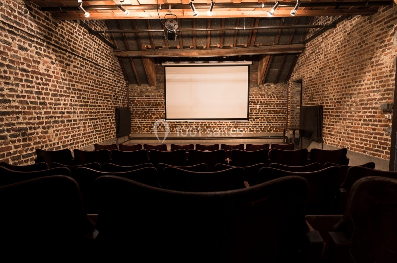 Location salle Linkebeek (Brabant flamand) - Ferme Holleken Hoeve #10 Salle de projection avec écran blanc, rangées de sièges en premier plan et murs en briques apparentes.