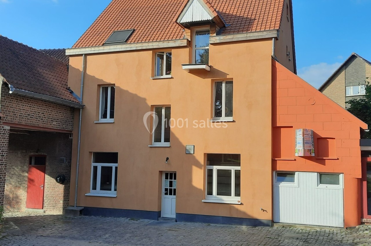 Location salle Linkebeek (Brabant flamand) - Ferme Holleken Hoeve #12 Façade d'une maison orange à trois étages avec toit en tuiles, entourée de bâtiments en briques et d'une cour pavée.