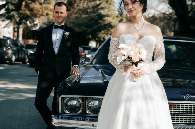 Une femme en robe de mariée tient un bouquet de tournesols près d'une voiture ancienne rouge, de nuit.