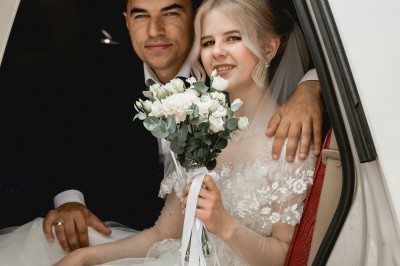 Une femme en robe de mariée tient un bouquet de tournesols près d'une voiture ancienne rouge, de nuit.
