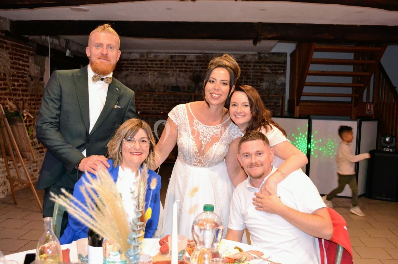 Un groupe de personnes souriantes posant autour d'une table lors d'une célébration dans une salle au décor rustique.