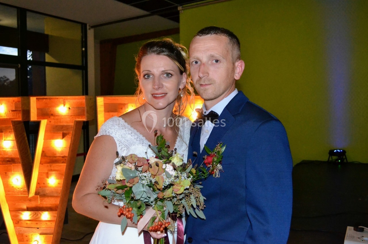 Un couple en tenue de mariage pose devant une décoration lumineuse dans un espace intérieur.