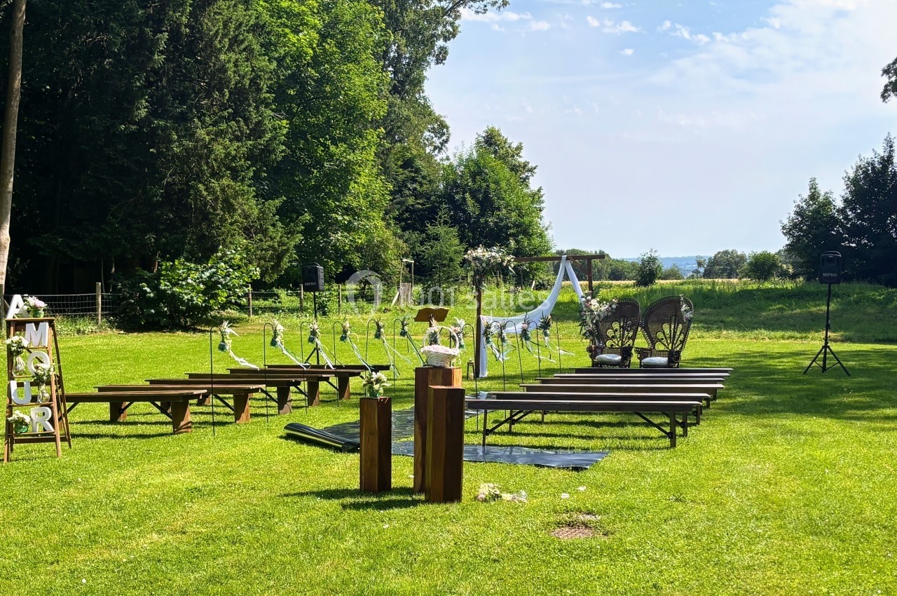 Chaises et bancs disposés en extérieur pour une cérémonie, avec arche décorée et verdure en arrière-plan.