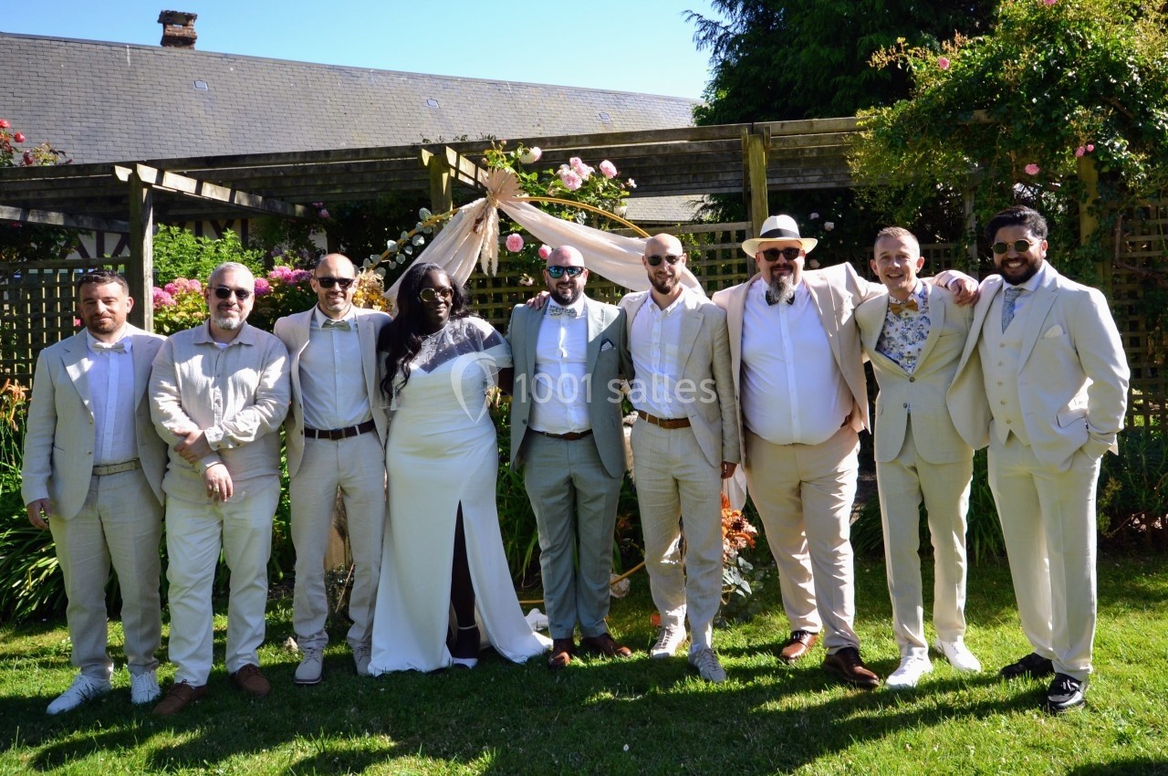 Un groupe de personnes en tenue élégante pose ensemble dans un jardin ensoleillé devant une arche décorée.