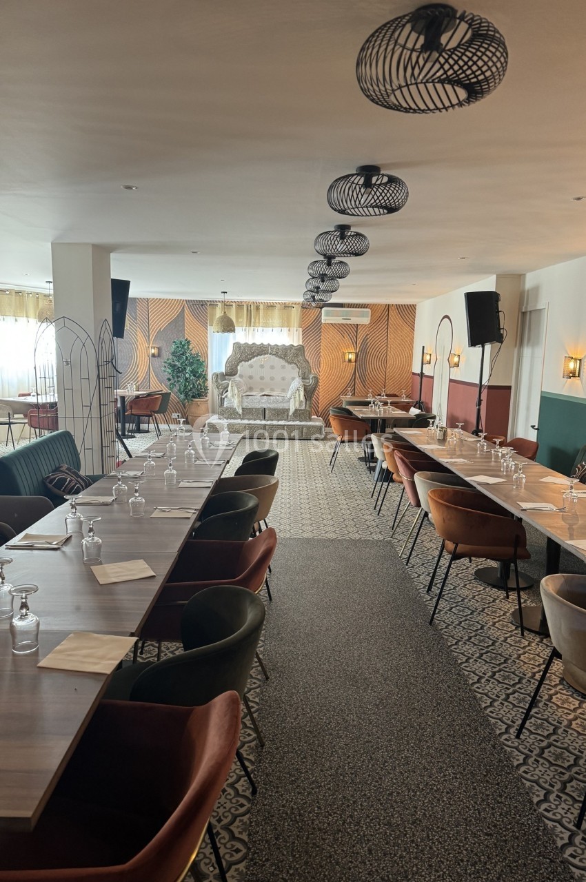 Salle de réception lumineuse avec tables alignées, chaises colorées et un canapé décoratif en fond.