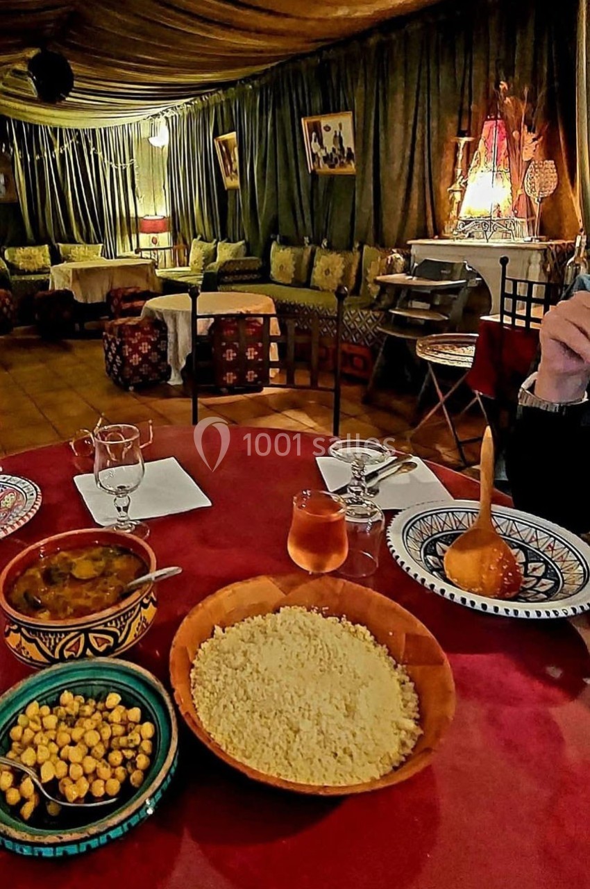 Repas marocain avec couscous, pois chiches, soupe et boissons, servi sur une table dans un décor traditionnel chaleureux.