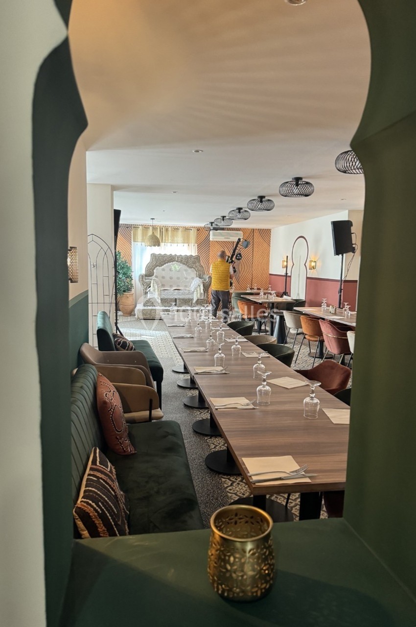 Salle de restaurant élégante avec longues tables dressées, décor chaleureux et éclairage tamisé.