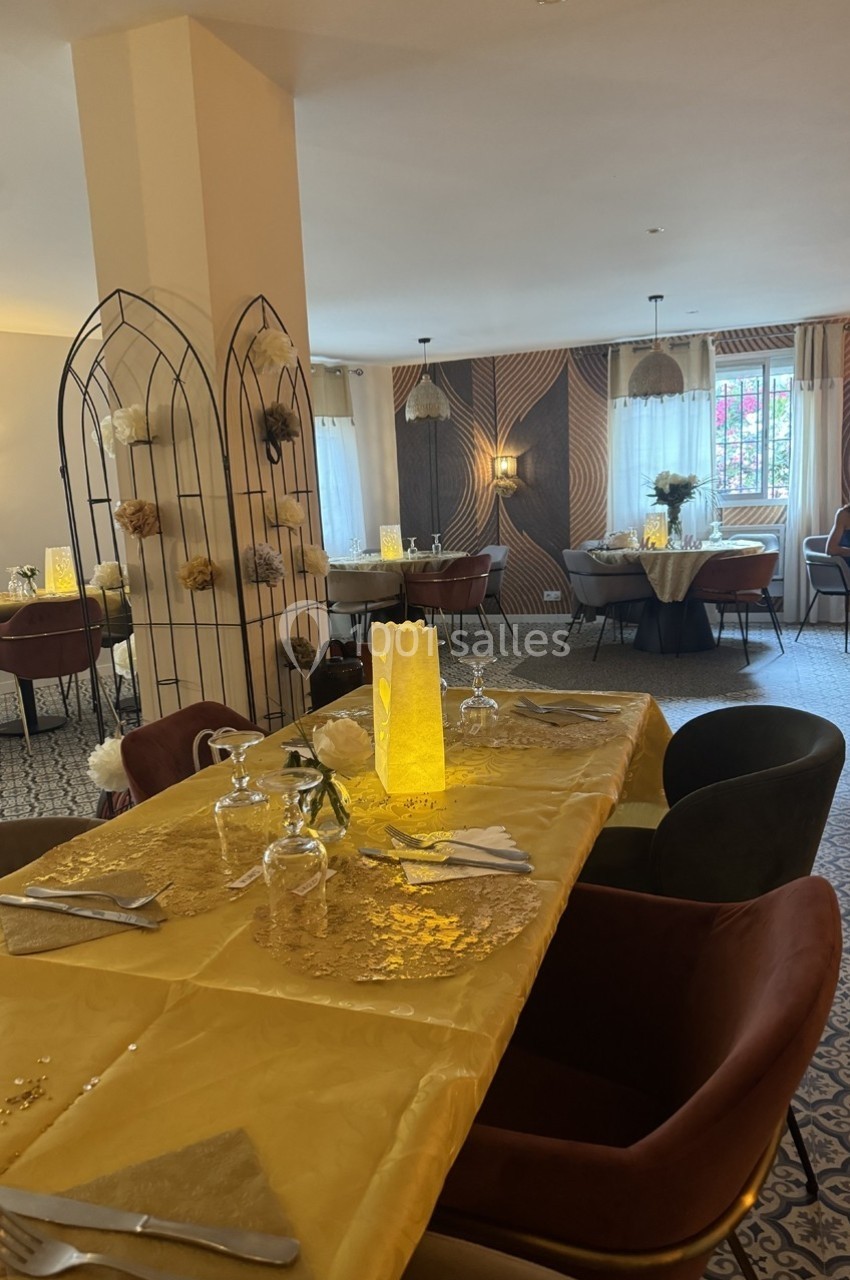 Salle de restaurant décorée avec des tables dressées, nappes jaunes, chaises colorées et lumière tamisée.