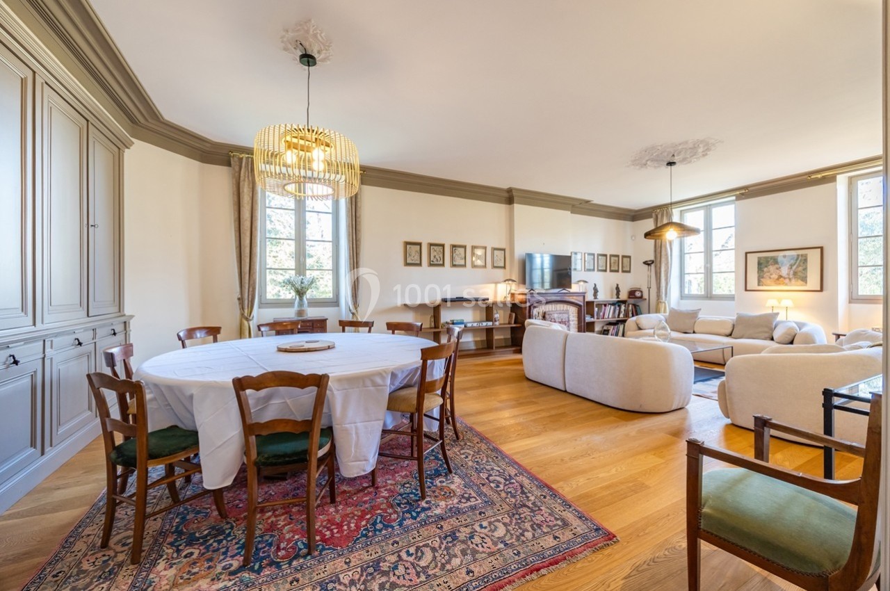 Salle à manger et salon lumineux avec parquet, table ronde, chaises en bois, canapé beige et décorations murales.