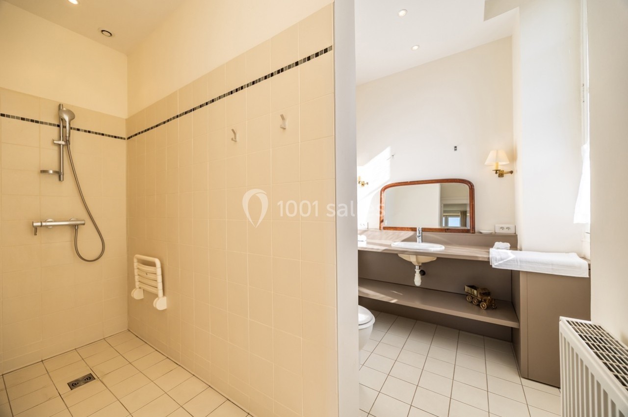 Salle de bain lumineuse avec douche à l'italienne, lavabo, miroir et murs carrelés dans des tons clairs.
