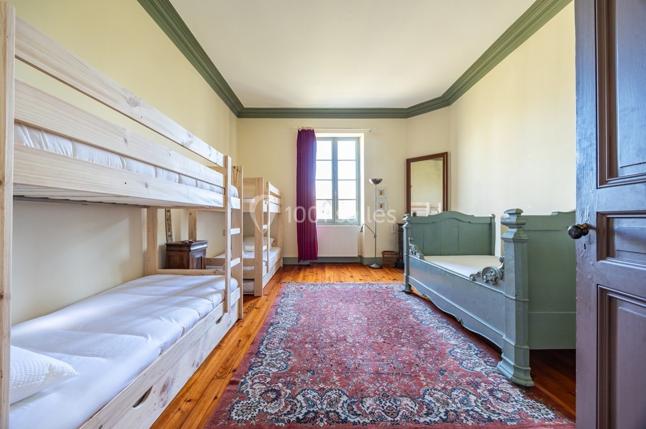 Chambre lumineuse avec lits superposés en bois, lit simple vert, tapis rouge et fenêtre donnant sur l'extérieur.