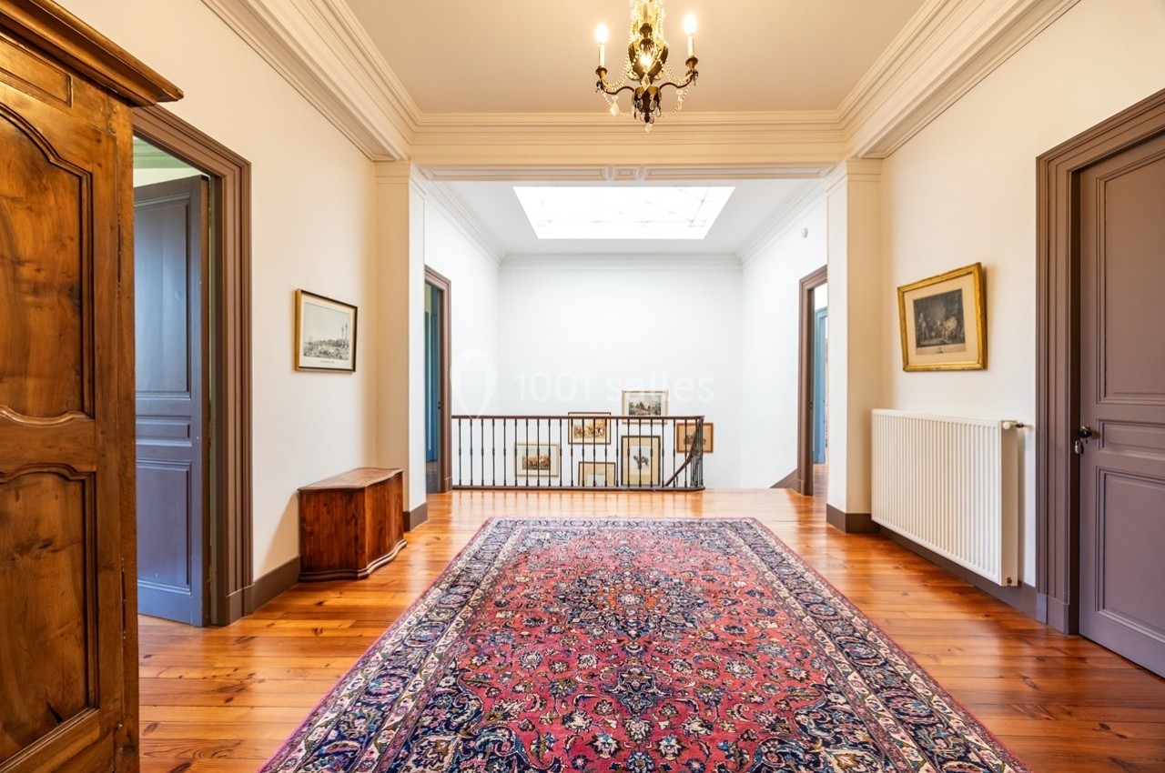 Vue d'un palier lumineux avec parquet, tapis oriental, rambarde en métal et meubles en bois.