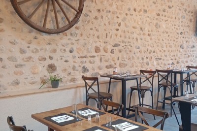 Table dressée avec verre, fourchette et serviette dans un restaurant rustique avec murs en pierre et menu en arrière-plan.