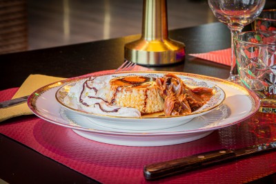 Coupe de dessert avec morceaux de fruits, glace, sauce chocolat et biscuit, posée sur une table avec serviette et verre.