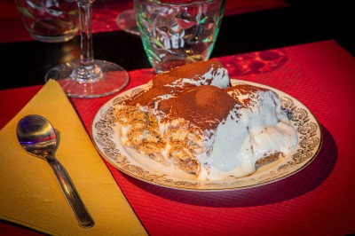 Coupe de dessert avec morceaux de fruits, glace, sauce chocolat et biscuit, posée sur une table avec serviette et verre.