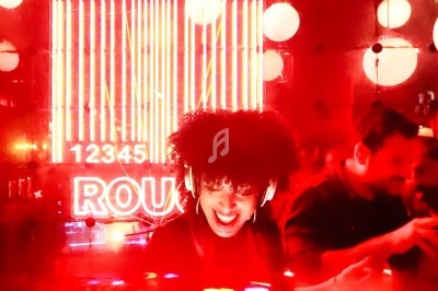 Femme souriante dans un bar éclairé par des néons rouges, avec des lumières suspendues en arrière-plan.