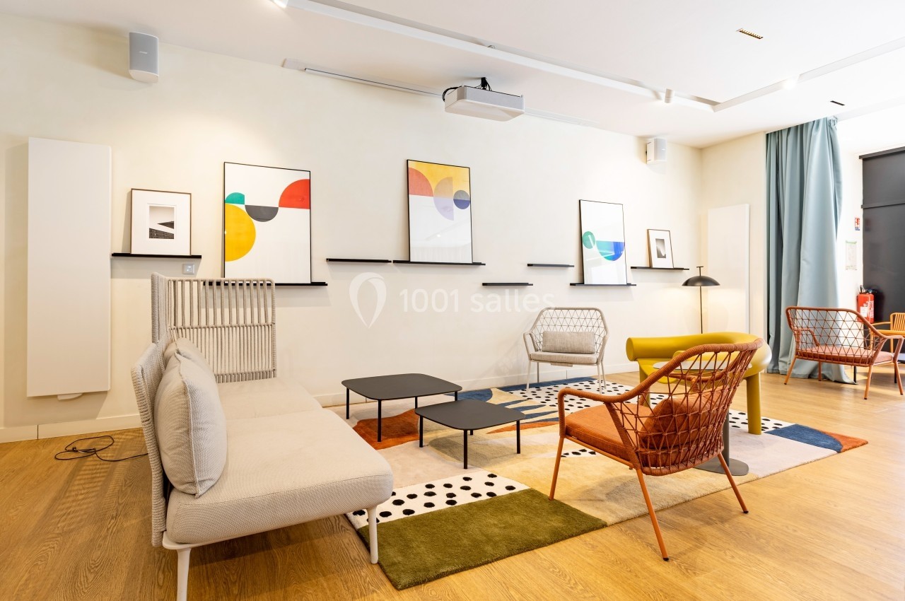Salon moderne avec mobilier design, tapis coloré, chaises en rotin et tableaux abstraits accrochés au mur.