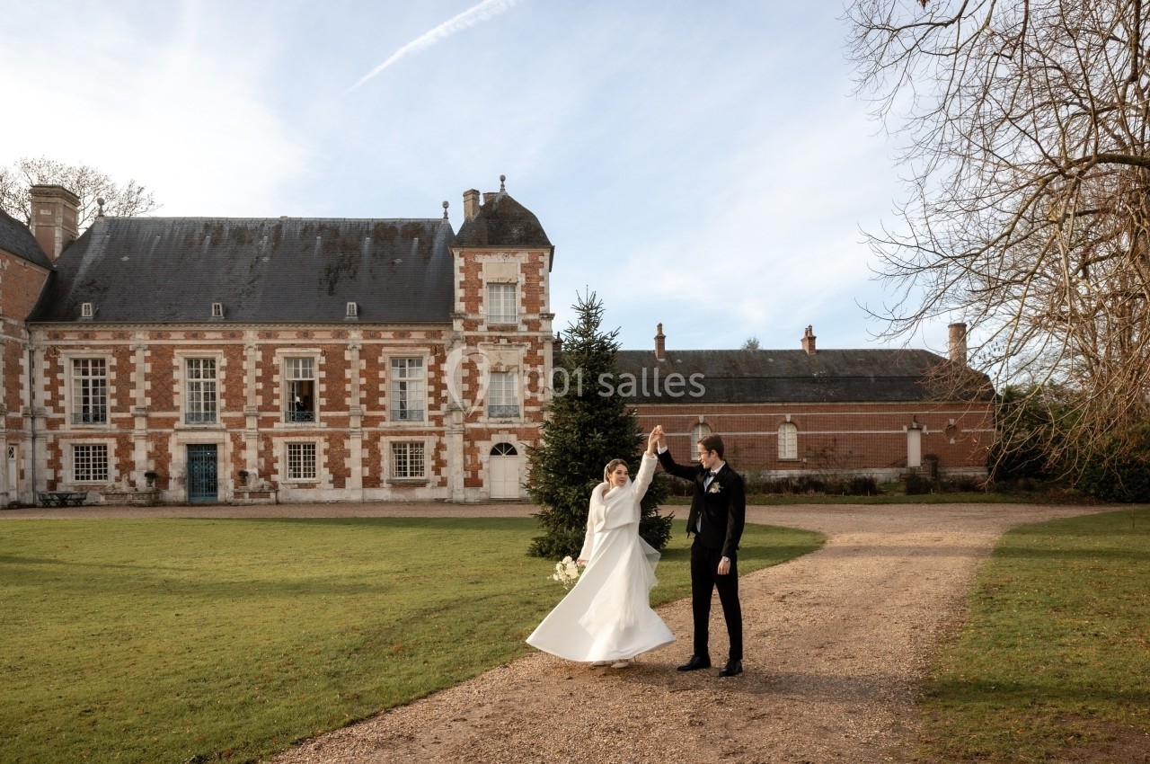 Un couple en tenue de mariage danse devant un château en briques rouges entouré d'un jardin.