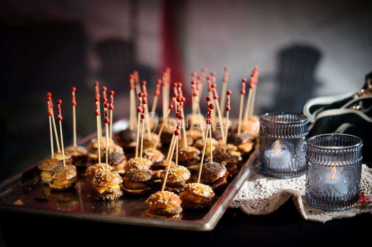 Plateau de mini-burgers avec des piques en bois, posé sur une table décorée de bougies et d'une nappe en dentelle.