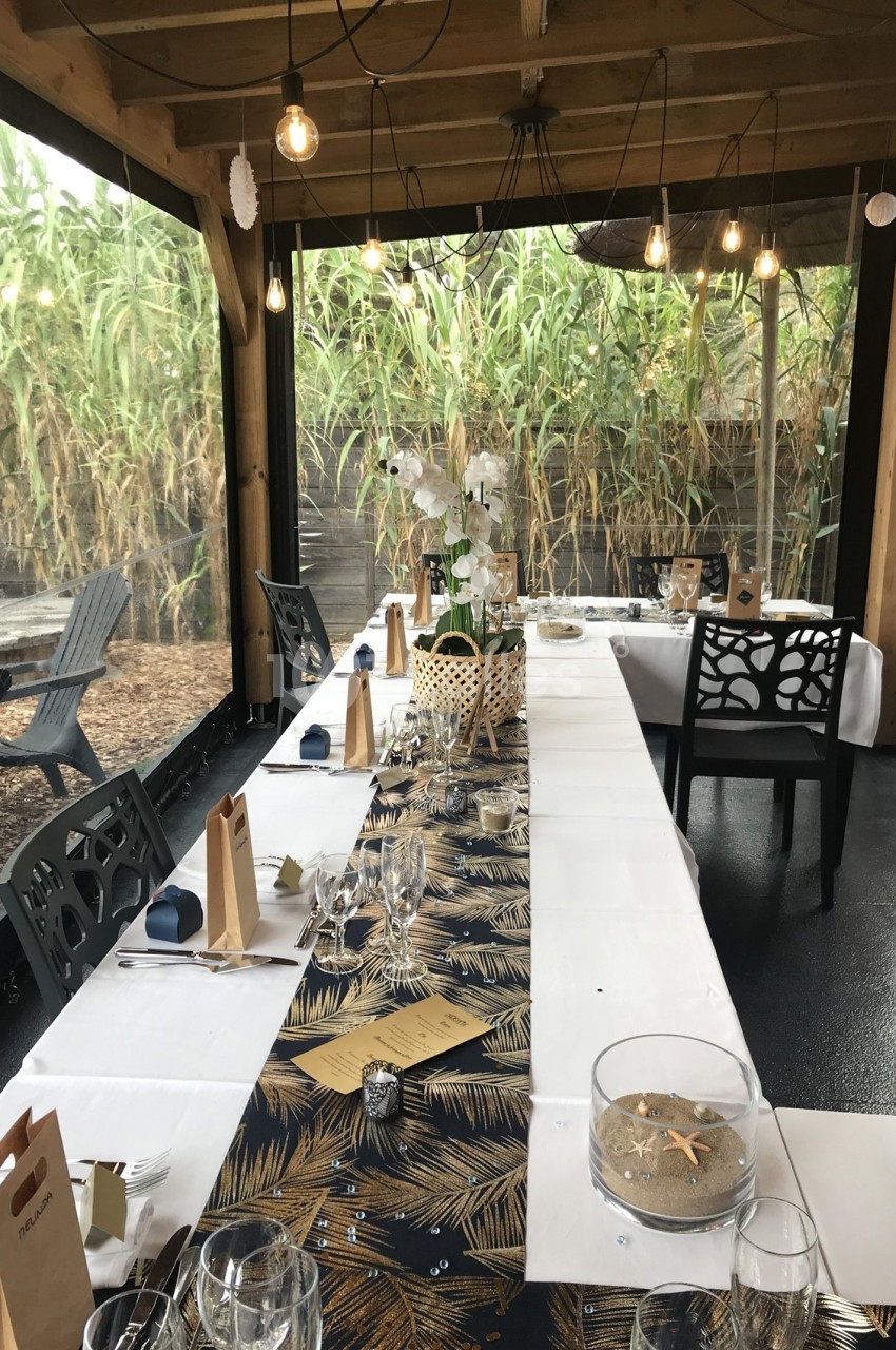 Table décorée pour un repas, avec nappes à motifs, vaisselle élégante et vue sur un jardin bordé de bambous.
