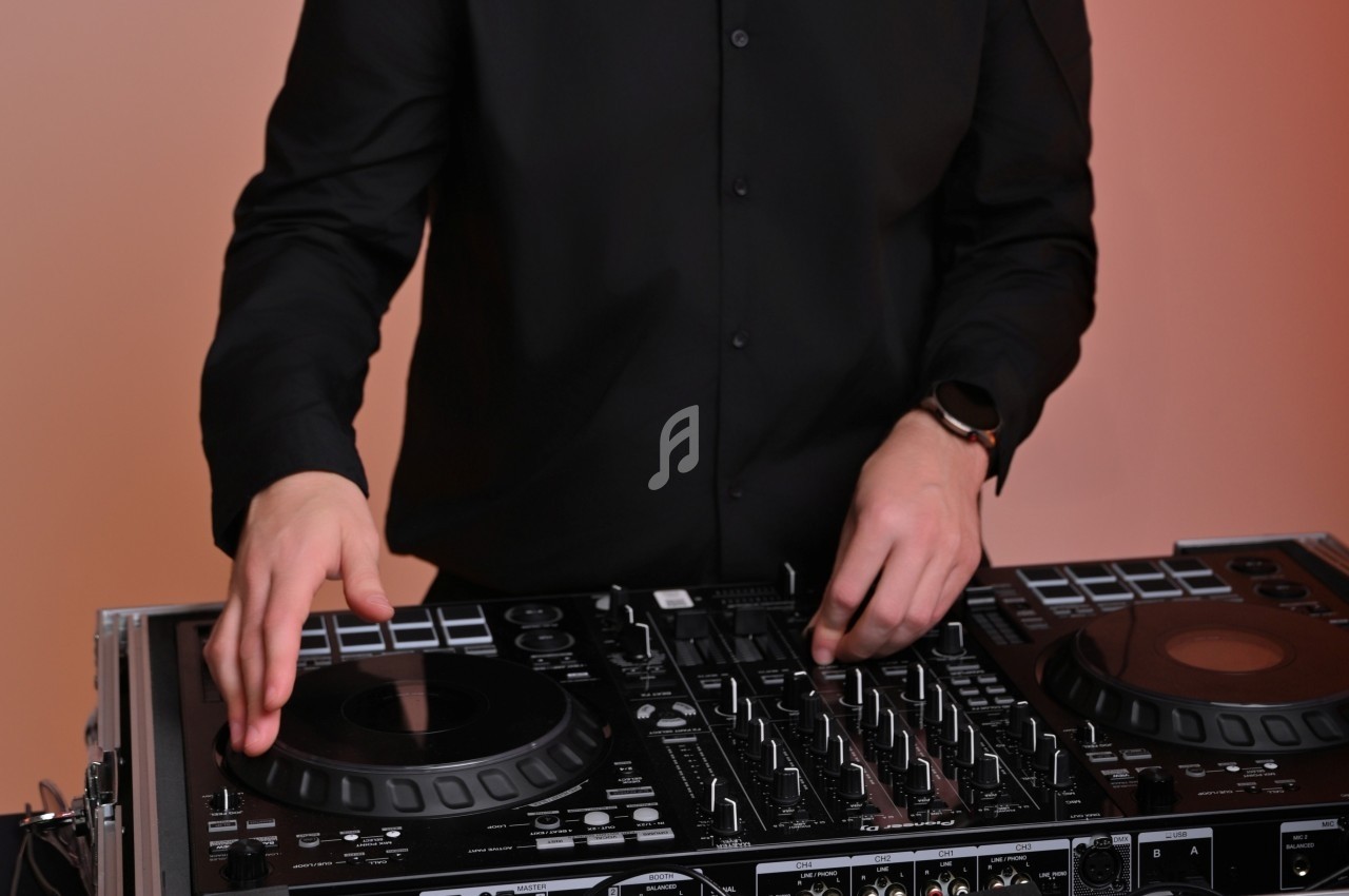 Personne en chemise noire utilisant une table de mixage DJ avec des platines et des commandes.