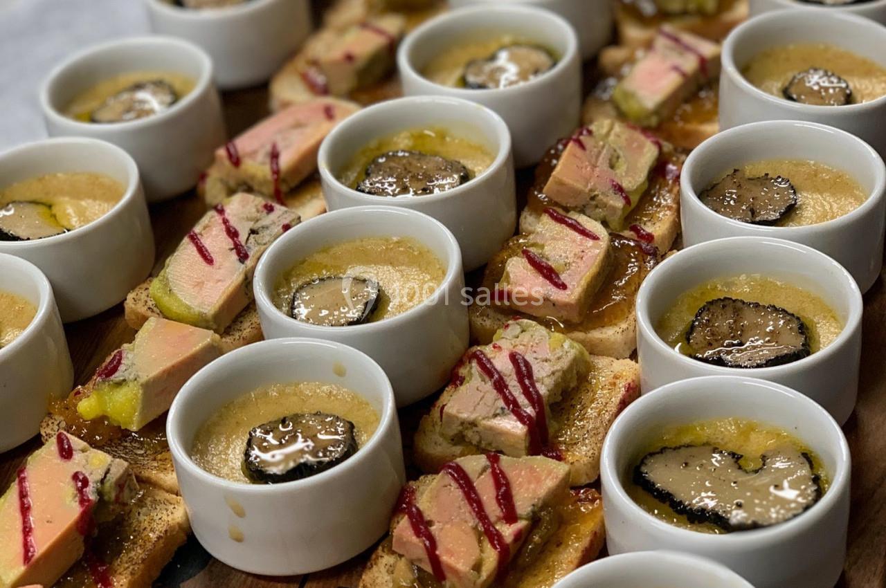Assortiment de verrines et toasts garnis de foie gras, truffes et sauces, disposés sur une planche en bois.