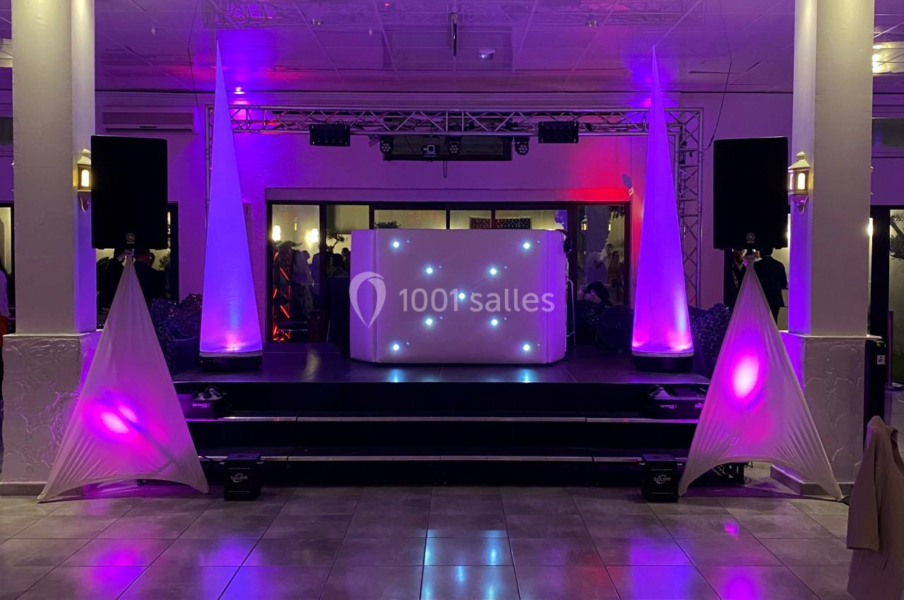 Scène de soirée avec une table de DJ illuminée, des projecteurs colorés et des décorations lumineuses violettes.