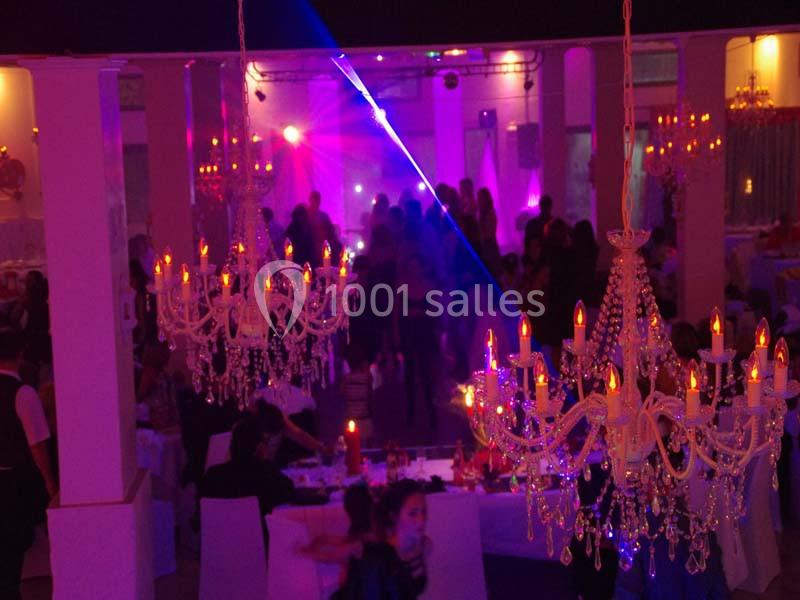 Salle de réception éclairée par des lustres, avec des invités dansant sous des lumières colorées.