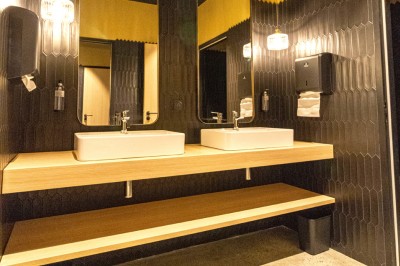 Douche moderne avec paroi vitrée, rideau à motifs noirs, sol en bois et porte blanche adjacente.
